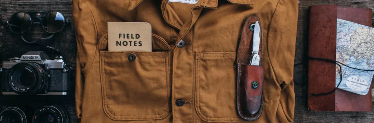 Veste de travail en toile, couteau de poche, appareil photo argentique et carnet de voyage
