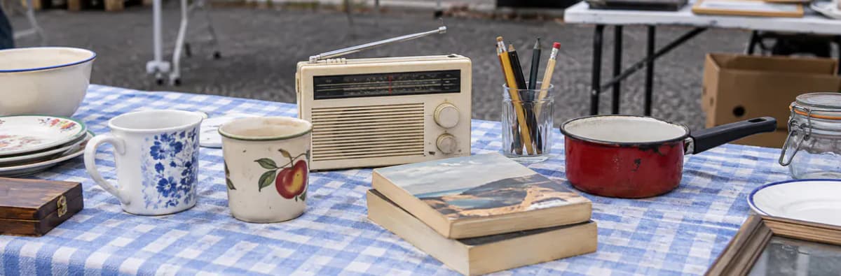 Table de vide-grenier avec radio ancienne, tasses en porcelaine, livres et casserole émaillée